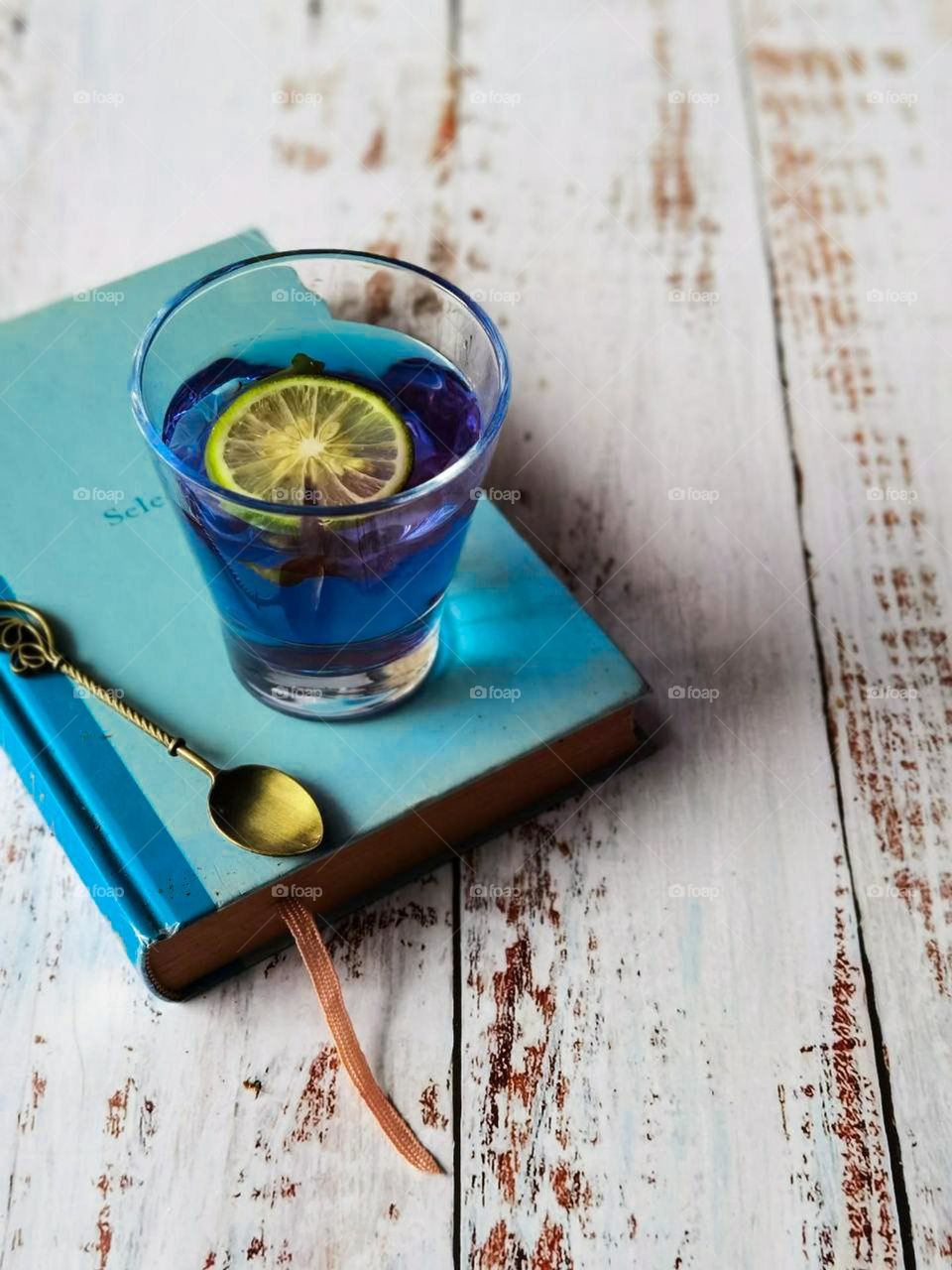 Butterfly pea tea with a slice of lemon on a blue book and a spoon beside it