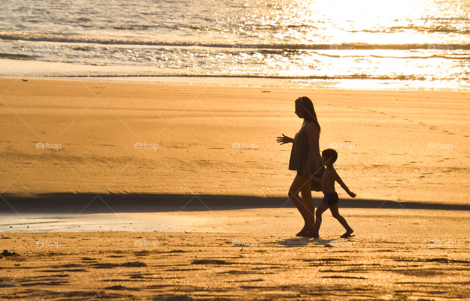 mother and son taking walk on beach during sunset