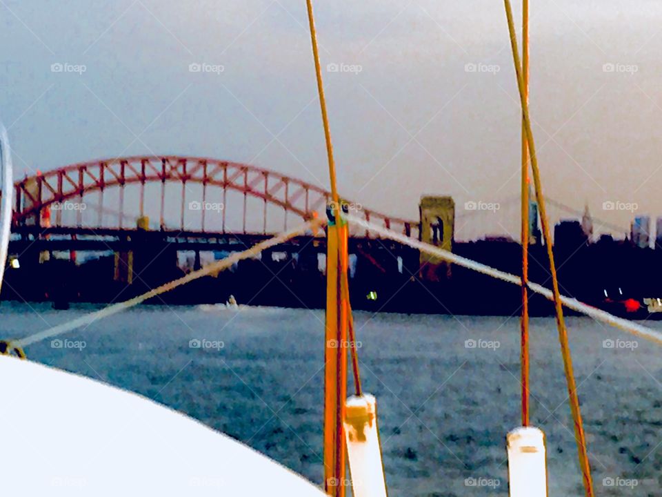 A arched red metal bridge leading across the East River seen from aboard our sailboat „Salvation“ traveling south towards Newtown Creek in LIC, Queens, NY around sunset or thereafter. 2017. Hypnotic Productions