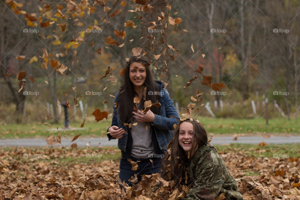 Two sister smiling in the park with falling autumn leaves