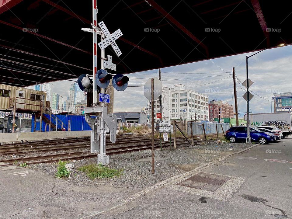 This is the “Long Island Railroad” crossing underneath the “Pulaski Bridge” at “Newtown Creek” in LIC, Queens. Two long red and white striped bars close off the pedestrian lane whenever there is a train approaching. 2023. Hypnotic Productions