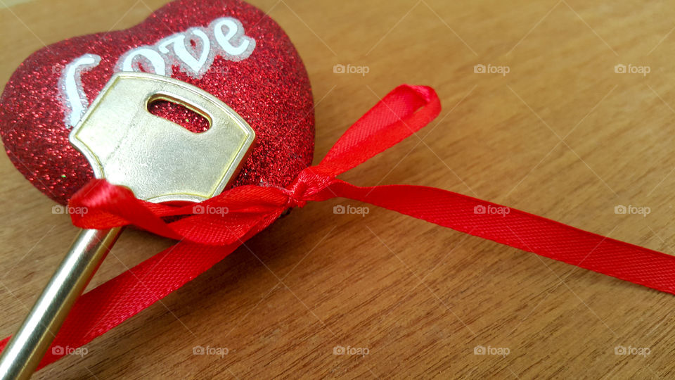 a red shiny heart with the word "love" written on it in white letters, a red ribbon is attached at the bottom, and a bronze key is visible from under the heart, copy space for text.