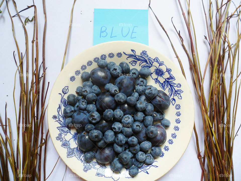 Berries of blueberries and plums on a white plate