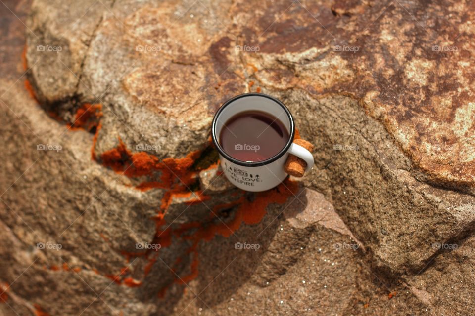 Black tea in a tin enameled mug on a piece of rock overgrown with lichen on a glacier in the mountains on a sunny day