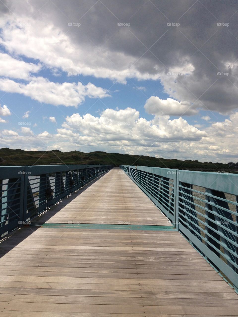 Sunny view of wooden walking bridge with metal sides towards vanishing point overhung with low clouds