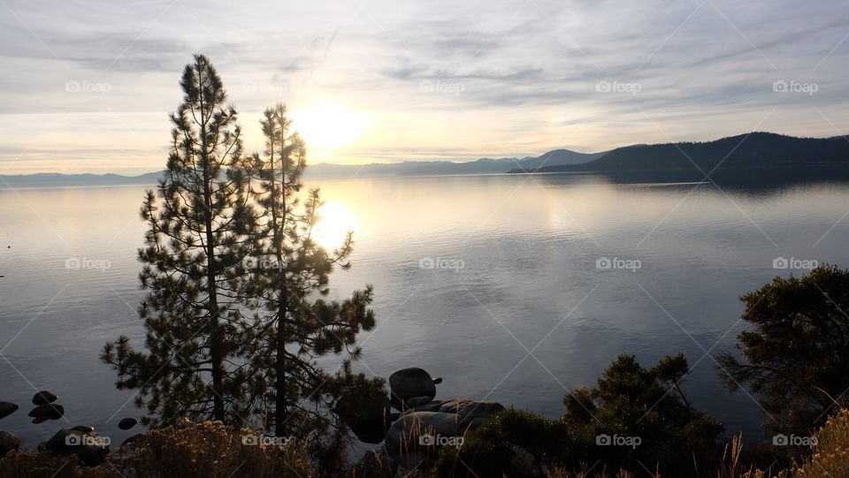 Evening on the lake. Sun setting on the still waters of a lake surrounded by hills