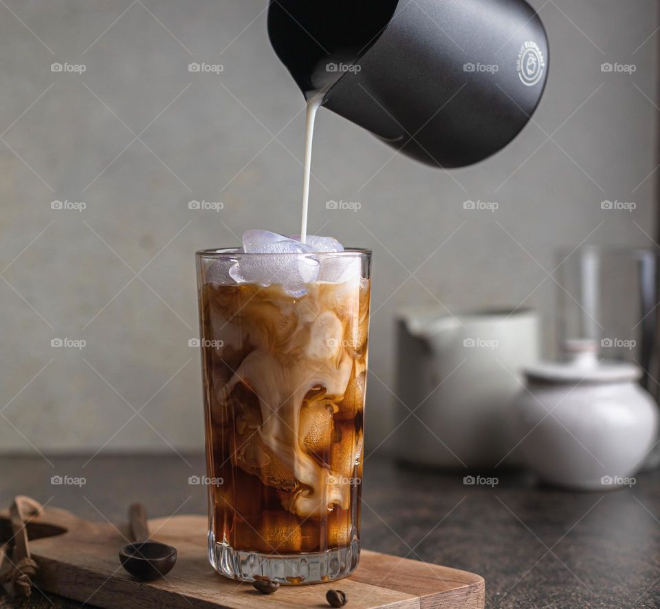 Pouring milk in a glass with iced coffee 