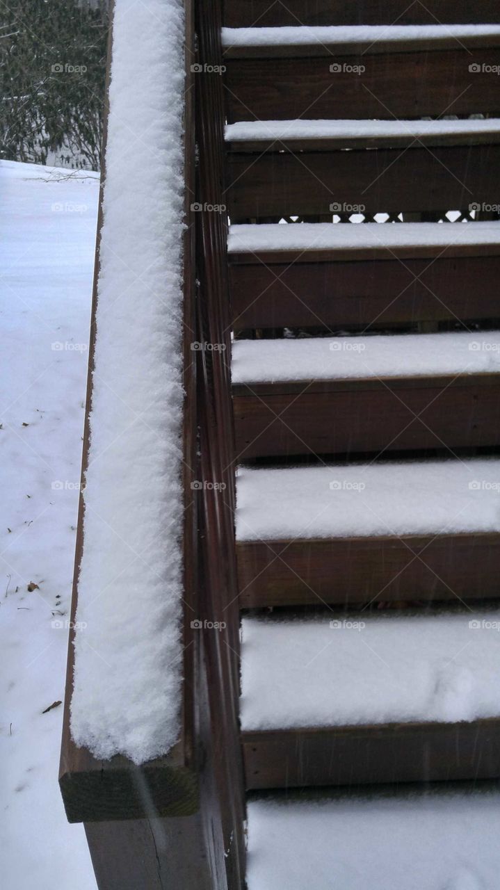 Close-up of snow covered stairs and railing made of wood with snow on the ground behind.