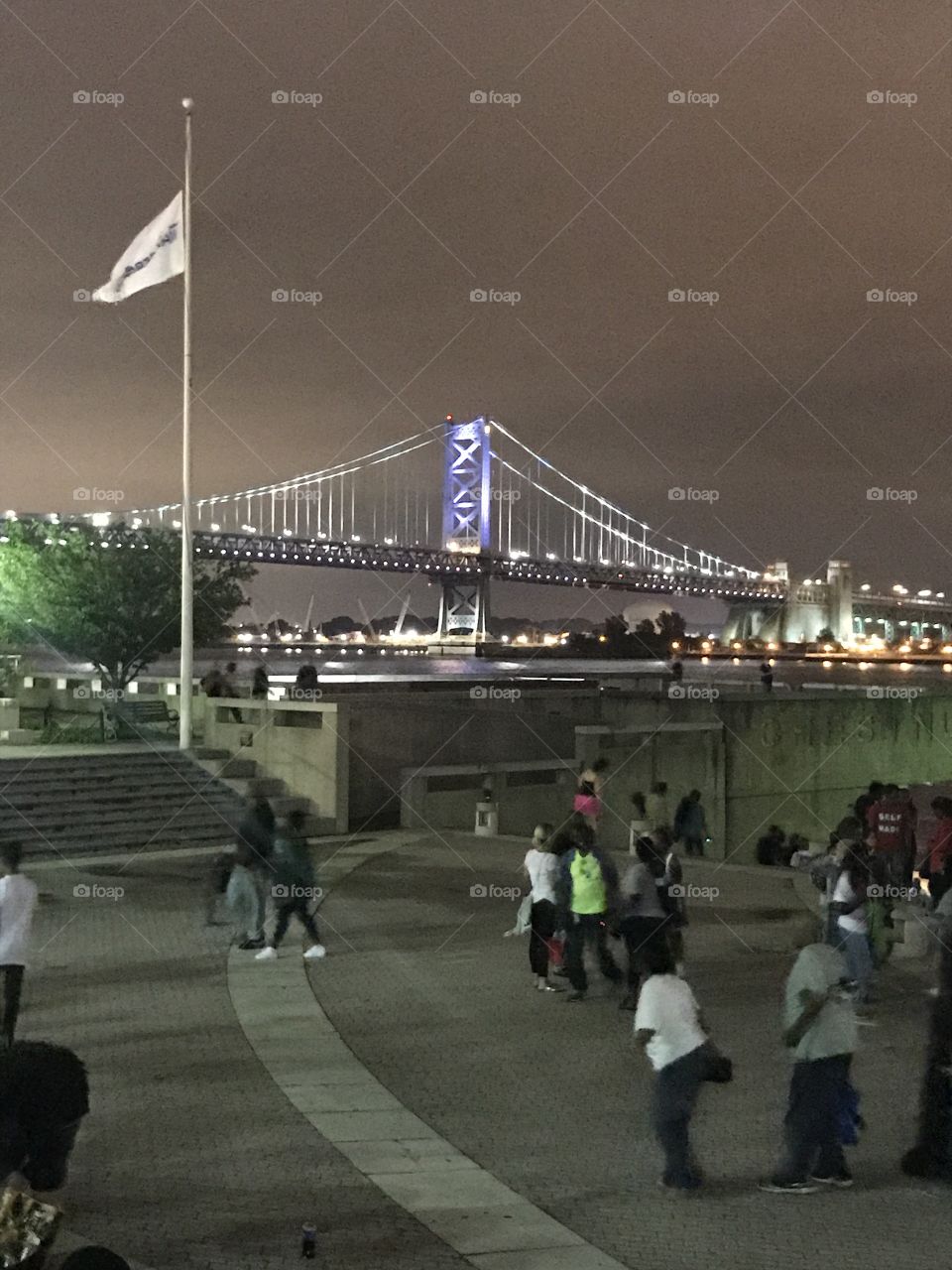 Benjamin Franklin Bridge at night from Penn’s Landing with flag