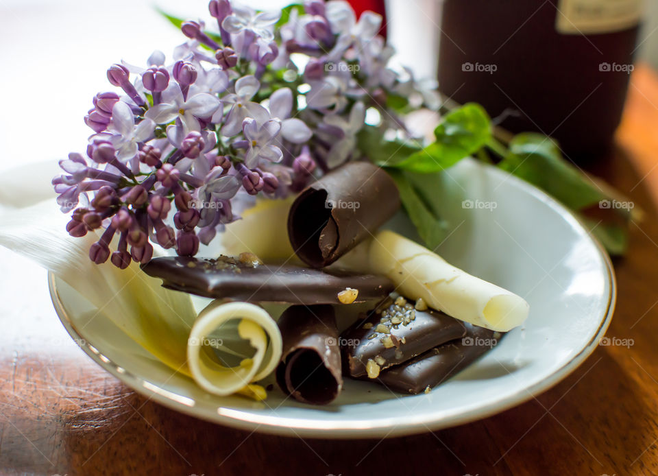 Plate of gourmet decadent dark chocolate pieces on wood table with fresh lilac flowers closeup epicure luxury foods rich in antioxidants photography