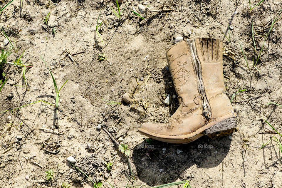 small dirty western cowboy boot on dry dirt ground