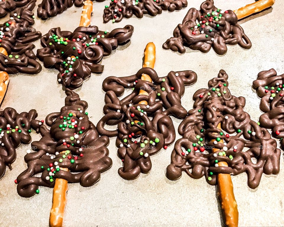 Chocolate drizzled over pretzel sticks in the shape of a a Christmas tree and then decorated with colorful sprinkles. A fun baking craft activity for all ages.