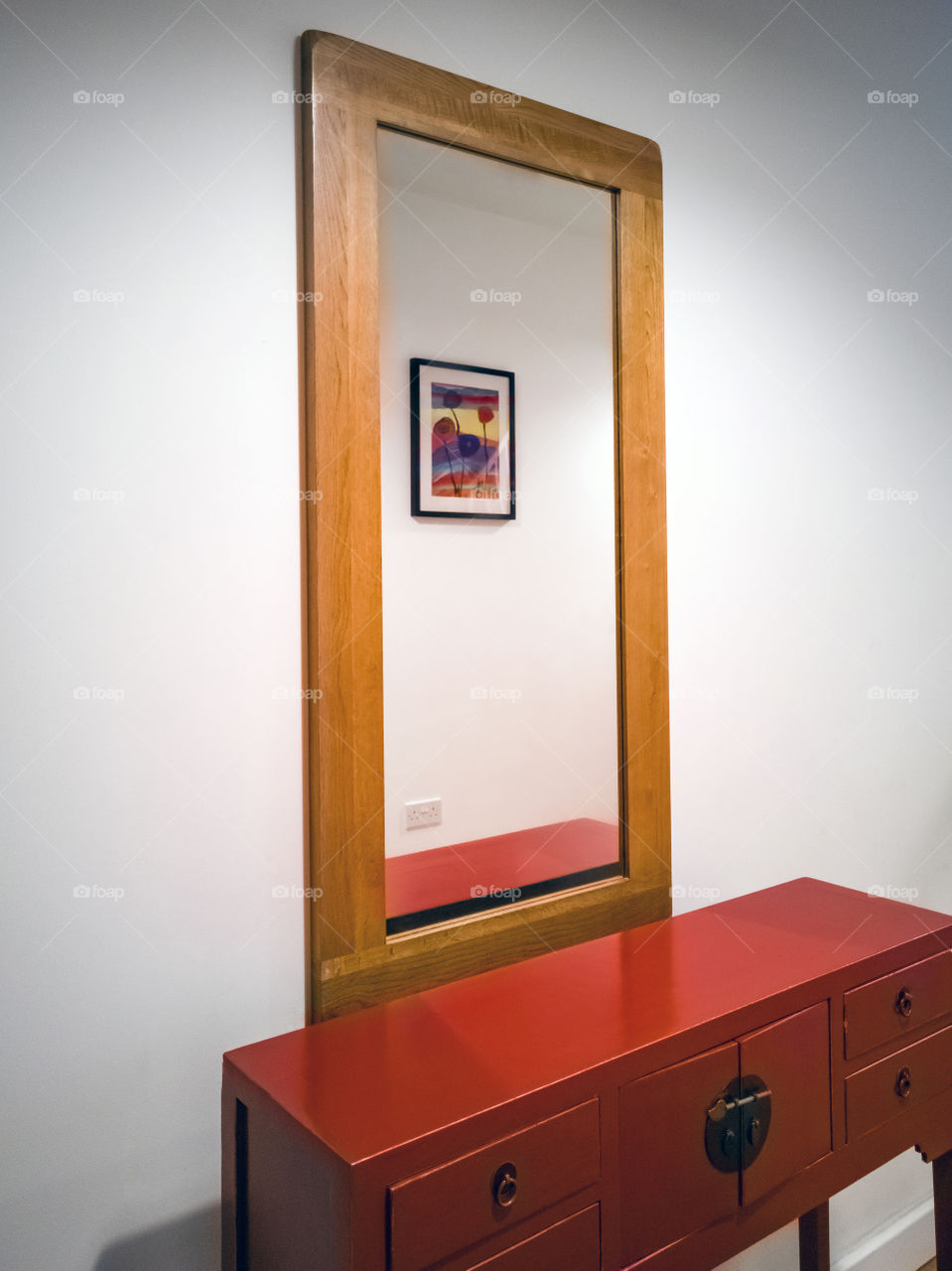 Rectangular wooden framed mirror reflects painting on the opposite wall.