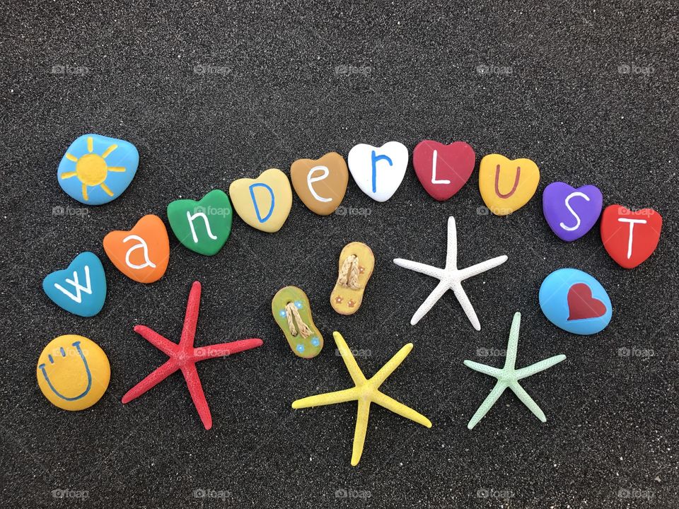 Wanderlust word with colored heart stones over black volcanic sand