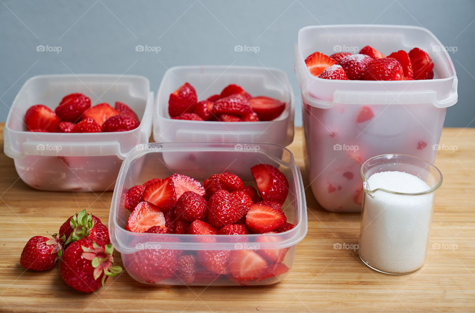 Fresh strawberries in plastic boxes ready for freezing and suger mug on wooden table.