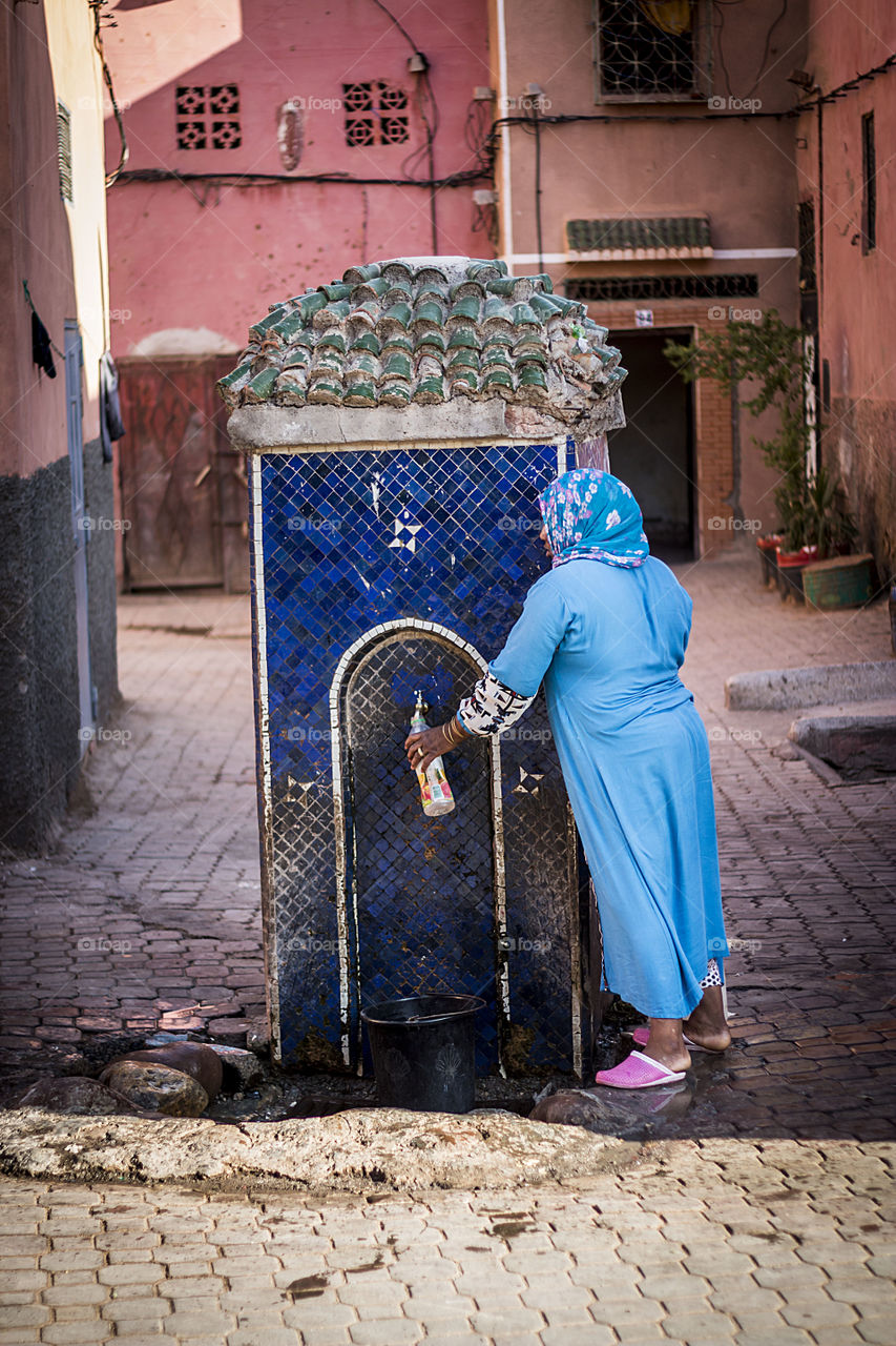 Lady in blue dress tapping water along the street