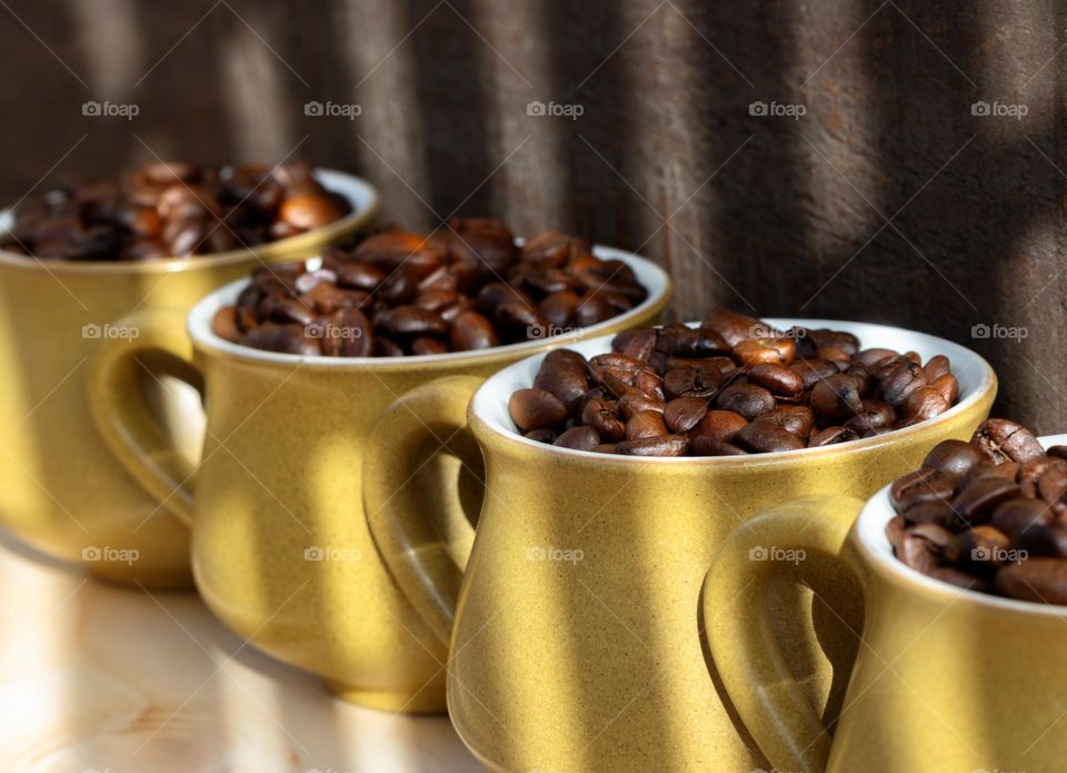 A row of 4 coffee cups, filled with coffee beans against a wood background with shadow lines across them