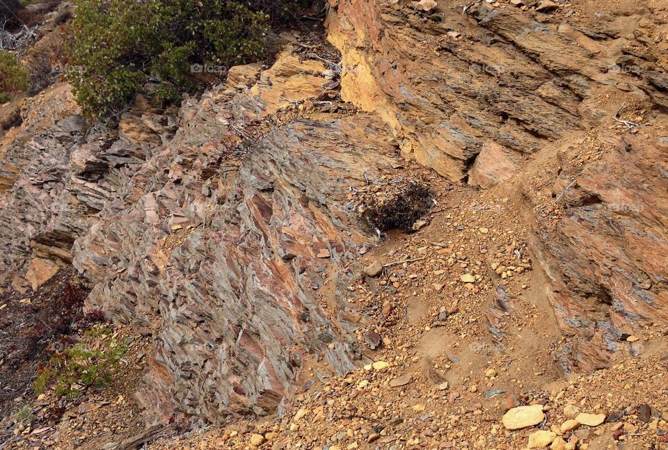 Layers of textured brown and red rock on the side of a mountain in Central Oregon on a sunny summer day. 