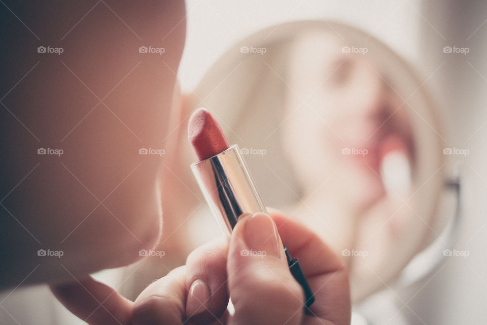 young woman putting on makeup in front of the mirror