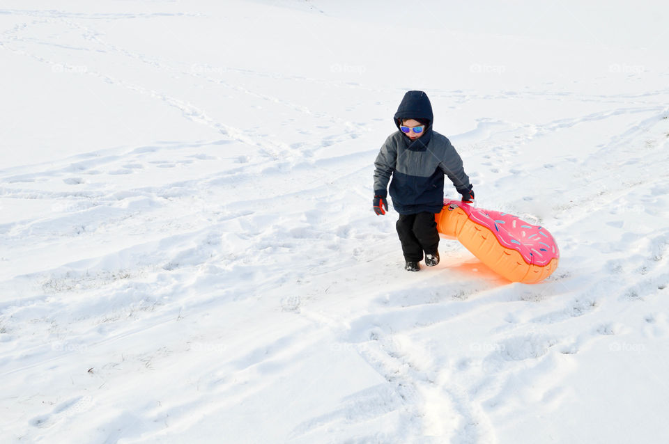 Young boy walking in the snow with a donut inner tube