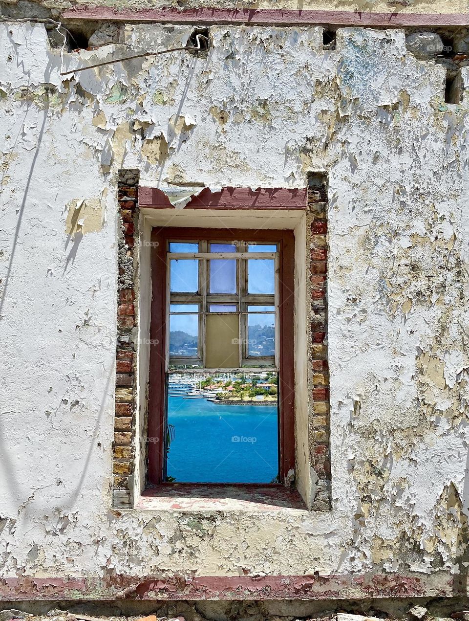 A window in a wall with peeling paint looking out over a harbor