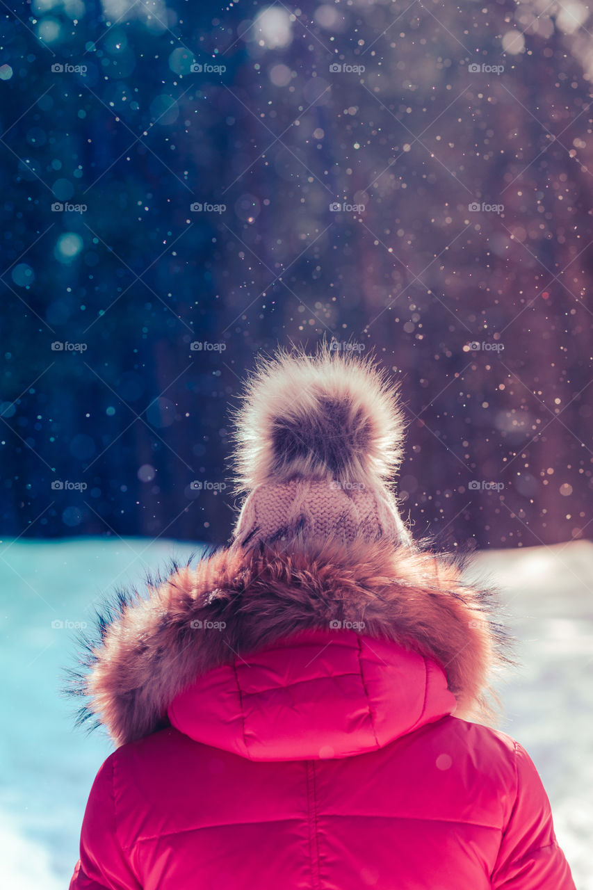 Close shot of woman walking outdoors on sunny snowy day in winter. Back view woman wearing winter coat and wool cap