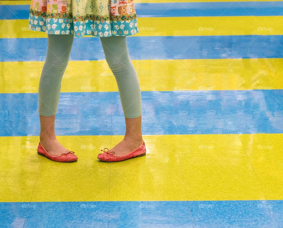 Colorful girl in bright dress standing on colorful striped floor - contrasts and shapes 