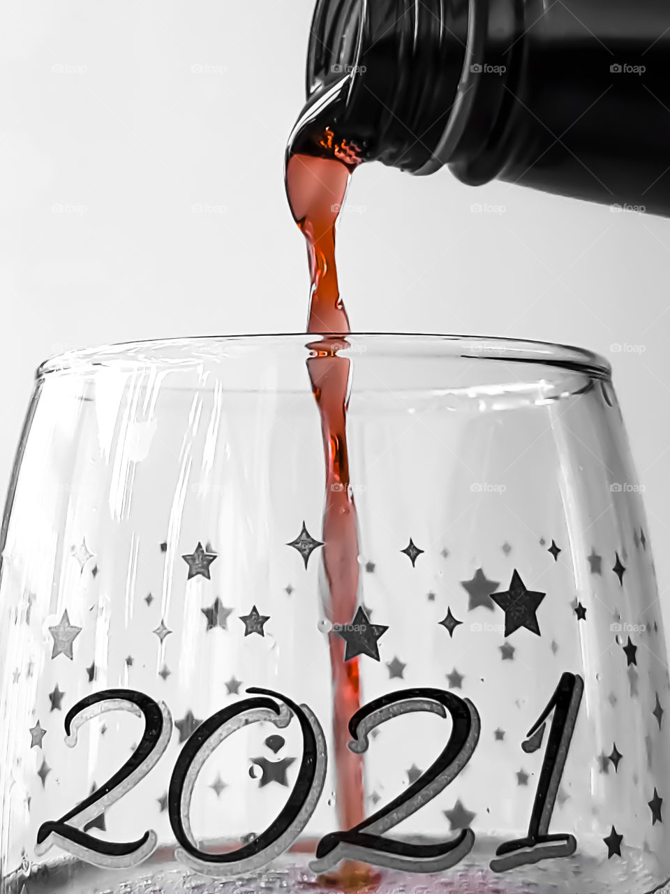 Pouring sparkling red wine in a 2021 wine tumbler glass to ring in the new year on a white background.