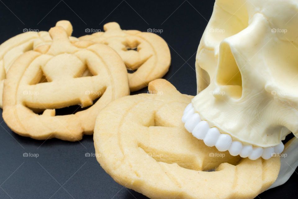 Skull biting a Halloween pumpkin-shaped cookie.