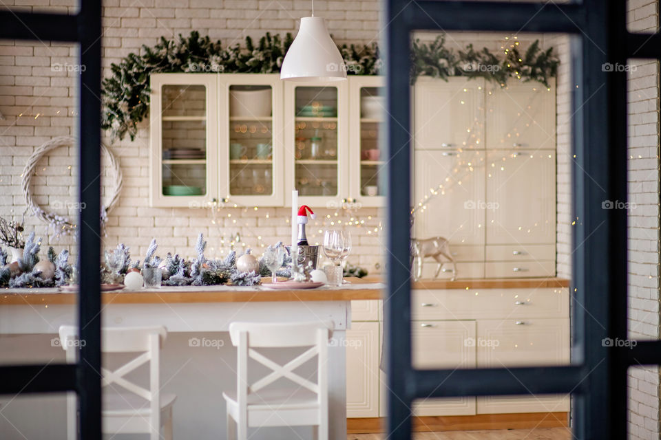 Festive winter cozy kitchen interior with garlands, decorations and gifts.  Christmas dinner at the decorated table.