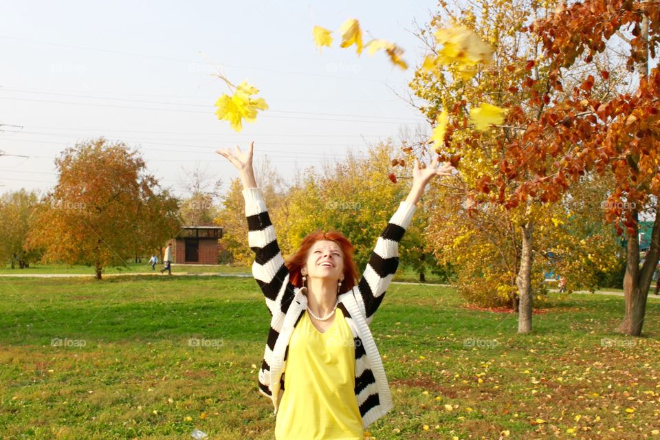Young woman throwing autumn leaf in air