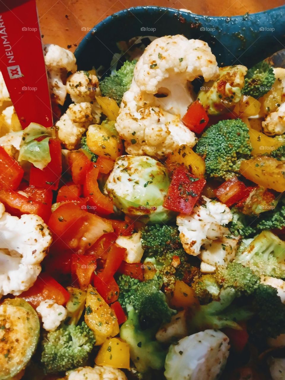 A bowl full of vegetables getting ready to roast with a blue spoon and red knife in the mixture.
