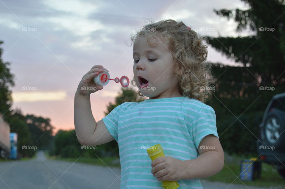 Little girl blowing soap bubbles outdoors