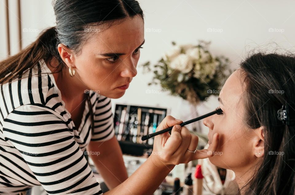 Beautician applying eyeshadow make-up on young woman