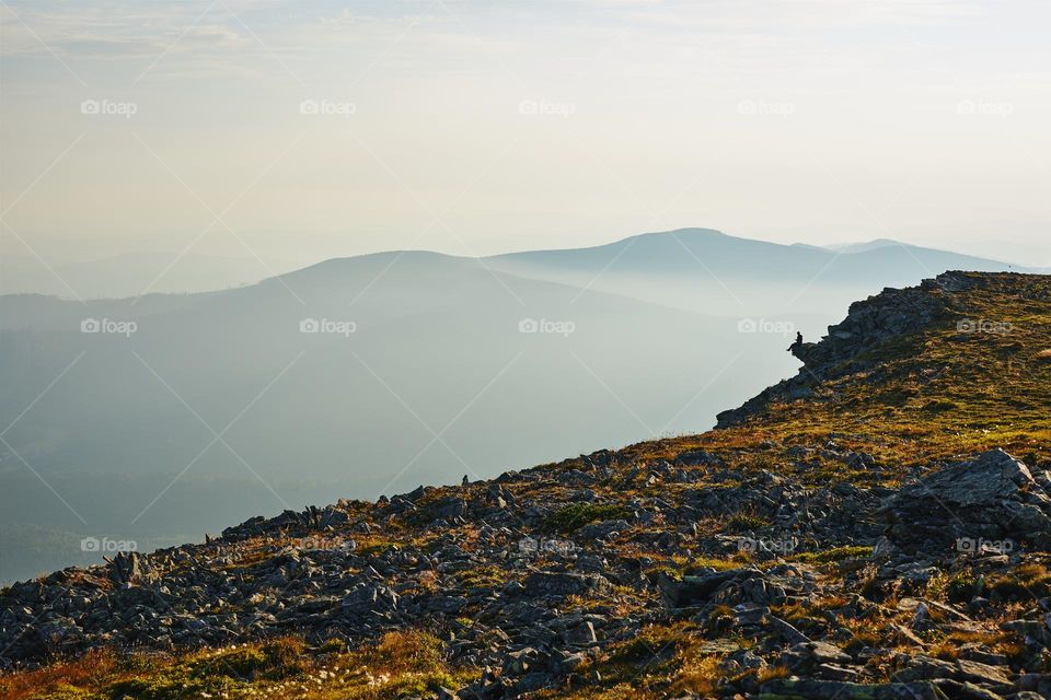 Man looking at sunrise. Mountains at sunrise. Man standing on peak. Natural mountain landscape with illuminated misty peaks, foggy slopes and valleys, blue sky with orange yellow sunlight. Amazing scene from Beskid Zywiecki in Poland