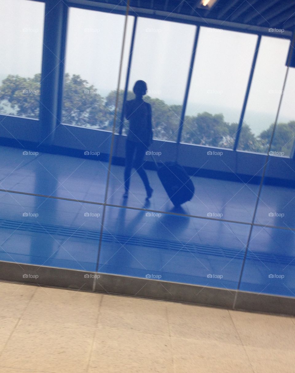 Reflection of a girl with a suitcase in a blue glass