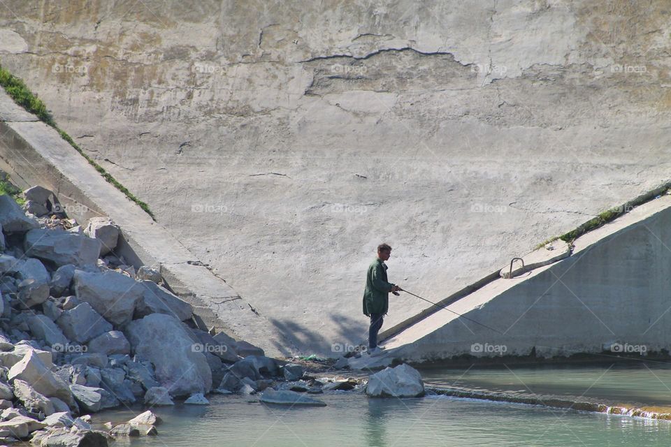 man on the river near the concrete building catching fish