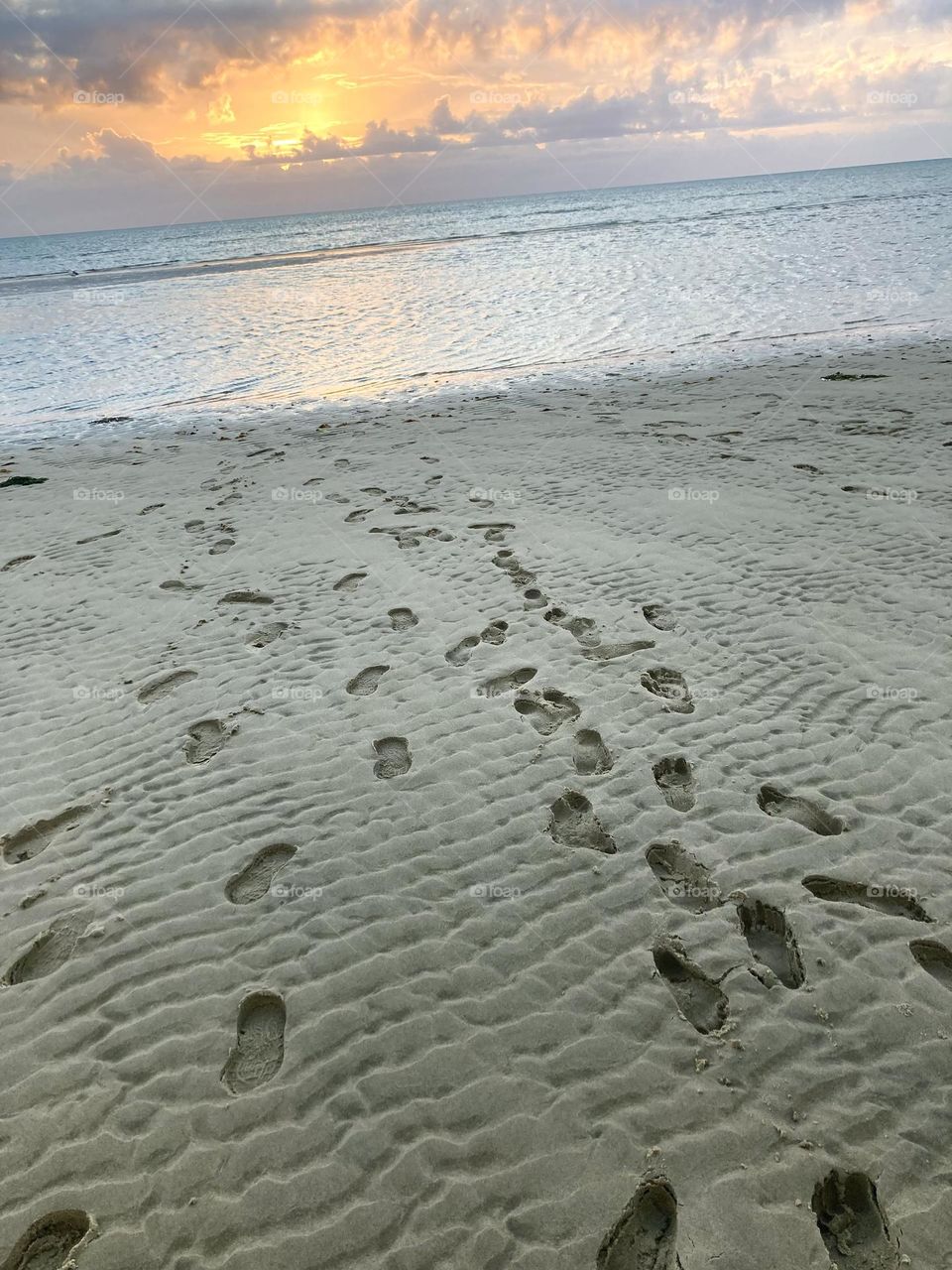 Footprints in the soft sand, strolling towards the vibrant sunset 