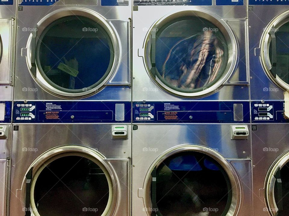 Washing machines at a laundromat in Long Island City, Queens, NY with their attractive silvery sheen set against the dark circular openings you can observe the “work in progress” through. 2021. Hypnotic Productions