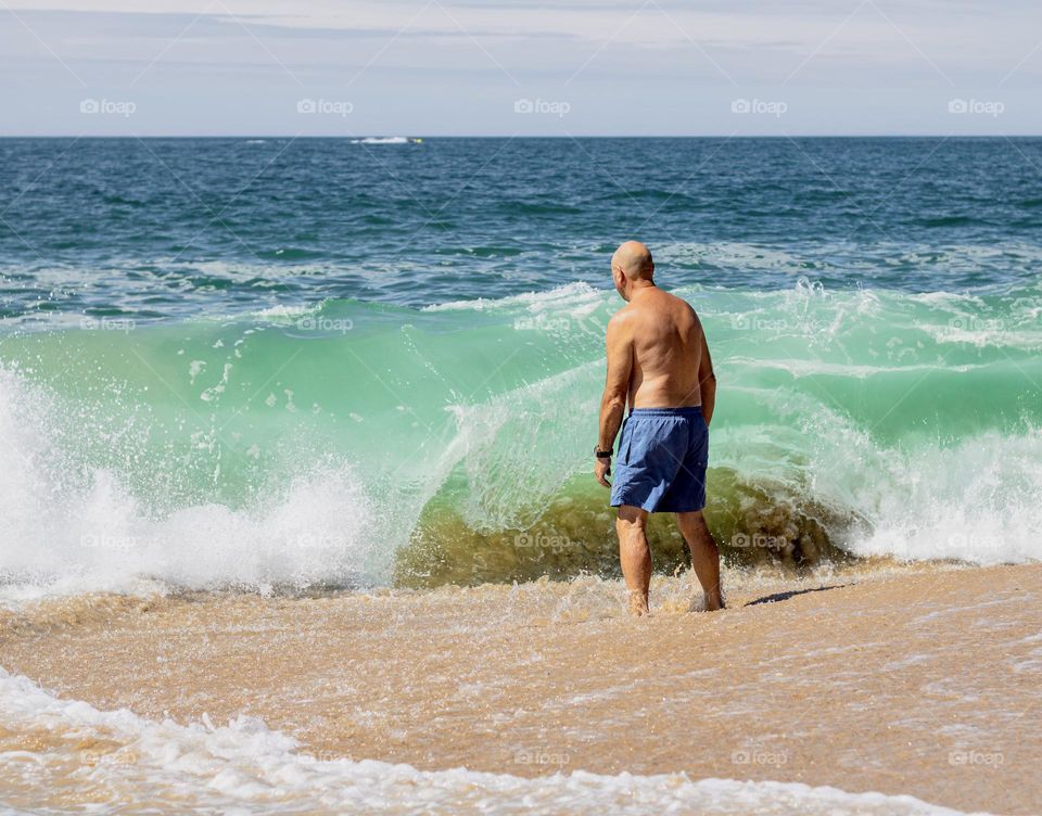 Man in blue swim shorts preparing to take a dip in the blue Atlantic Ocean 