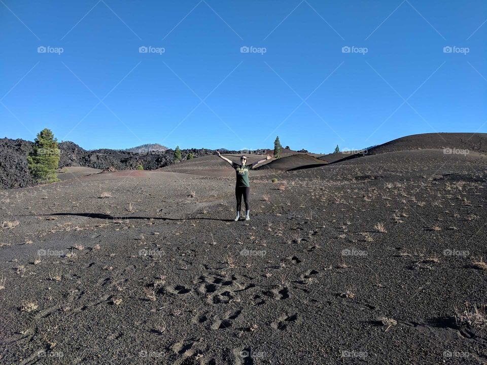 Person (Woman Wearing Green North Dakota State University Shirt) Holding Her Hands and Arms Up in Joy on Volcanic Ash at Cinder Cone in California
