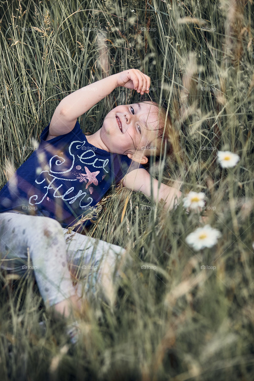 Little happy girl playing in a tall grass in the countryside. Candid people, real moments, authentic situations