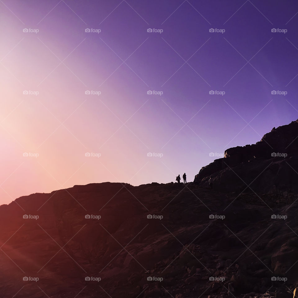 Silhouettes of two people hiking with backpack at the rock at early sunrise morning 