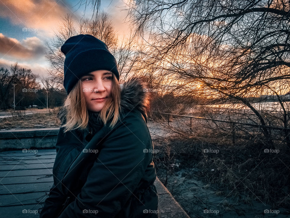 Portrait of a girl in warm clothing sitting at the beach during a golden sunset.