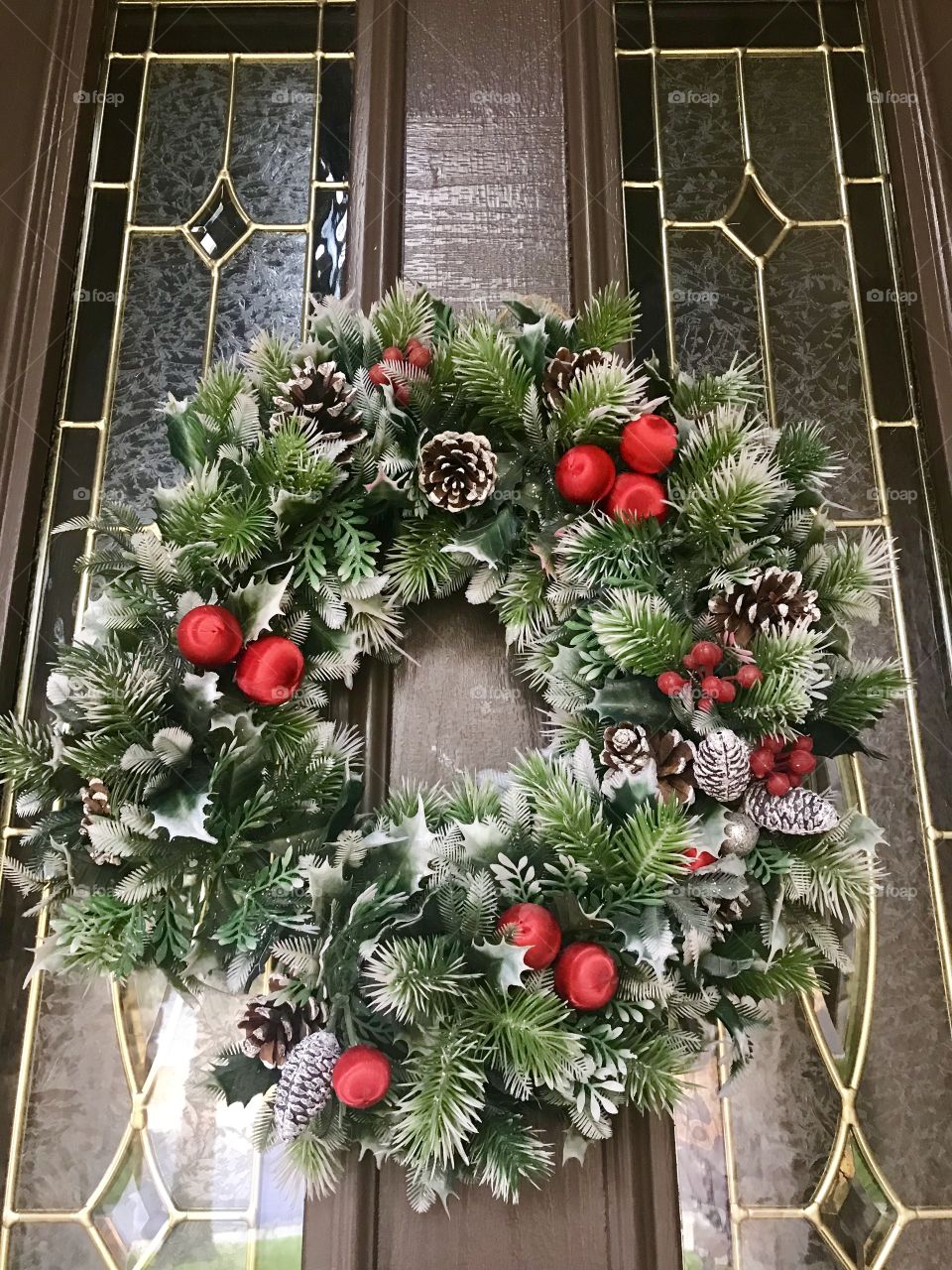 A Beautiful green Christmas wreath with red bulbs pinecones and berries displayed on the front door against glass windows. USA, America