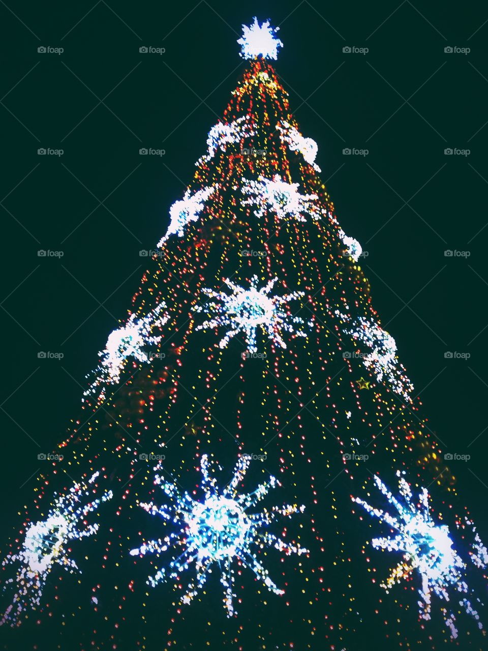 Bright colored illumination on artificial Christmas fir tree in the evening on black sky background in Moscow, Russia