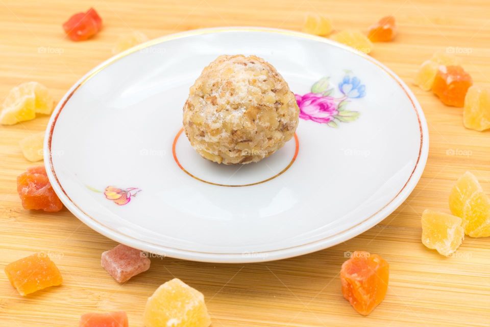 Plate with a panellet on a wooden surface surrounded by cubes of dried fruits. Panellets are traditional sweets for All Saints' Day in Catalonia, the Balearic Islands, Levante and Aragon.