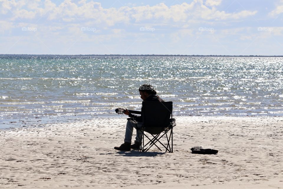 Singer guitarist sitting alone on remote beach playing and singing 