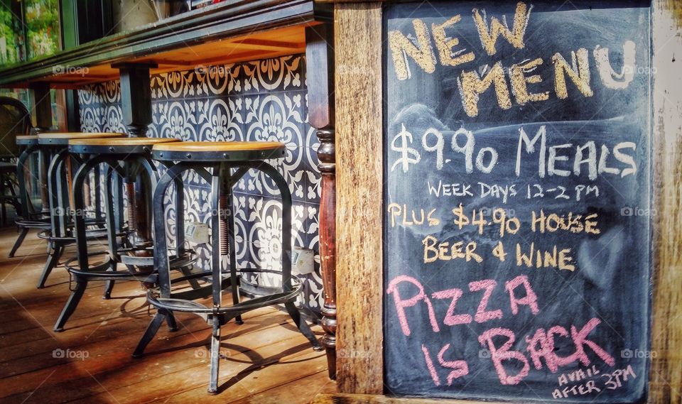 New menu items handwritten using chalk on a board placed outside a restaurant. It sports some outdoors seats.