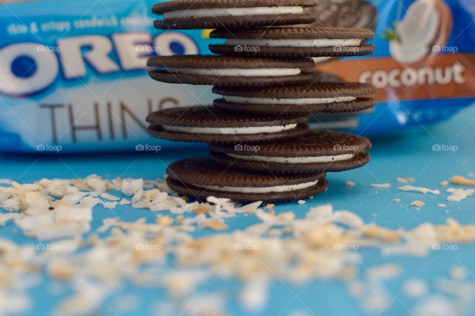 A stack of coconut Oreo thin cookies on a blue background with coconut shreds